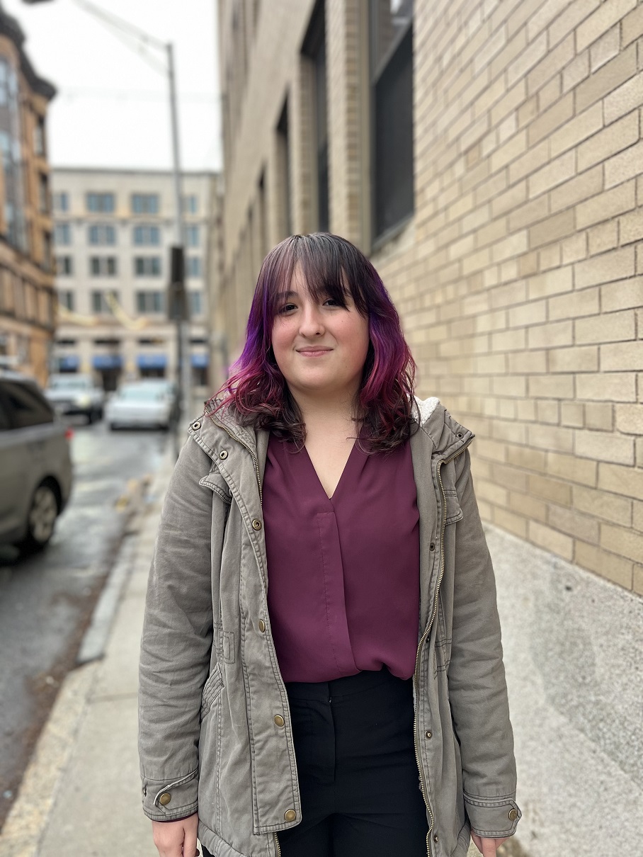 young woman with purple highlights in her hair and bangs, standing outside