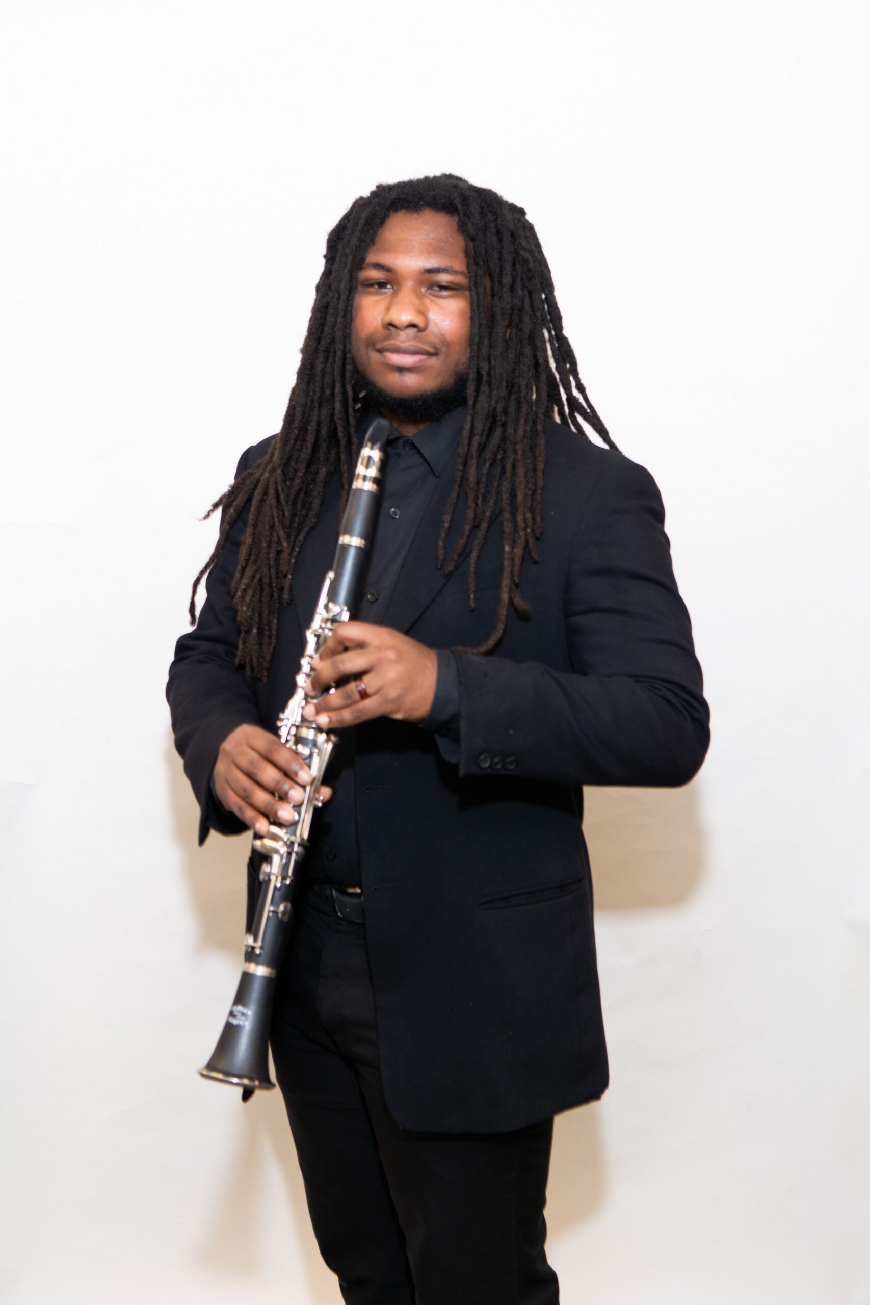 A young man with long dreads in a suit holding a clarinet