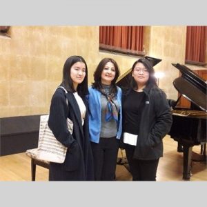 Marineh Kirakosyan posing with her students in front of a piano in Robyn Newhouse Hall
