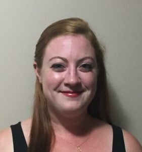 Headshot of Rachael James, against gray wall, smiling and showing shoulders and above