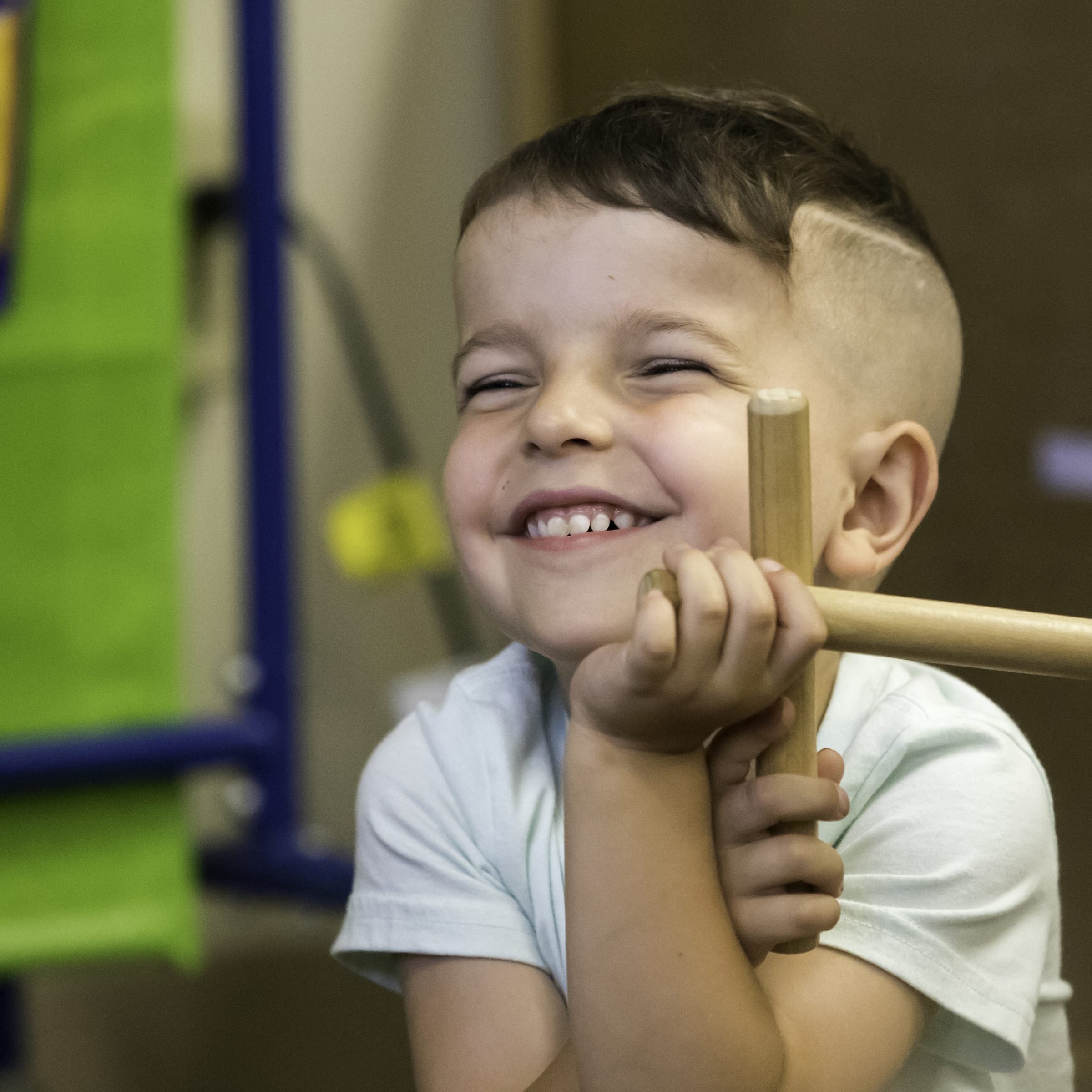 Prelude student smiling, holding wooden claves/rhythm sticks