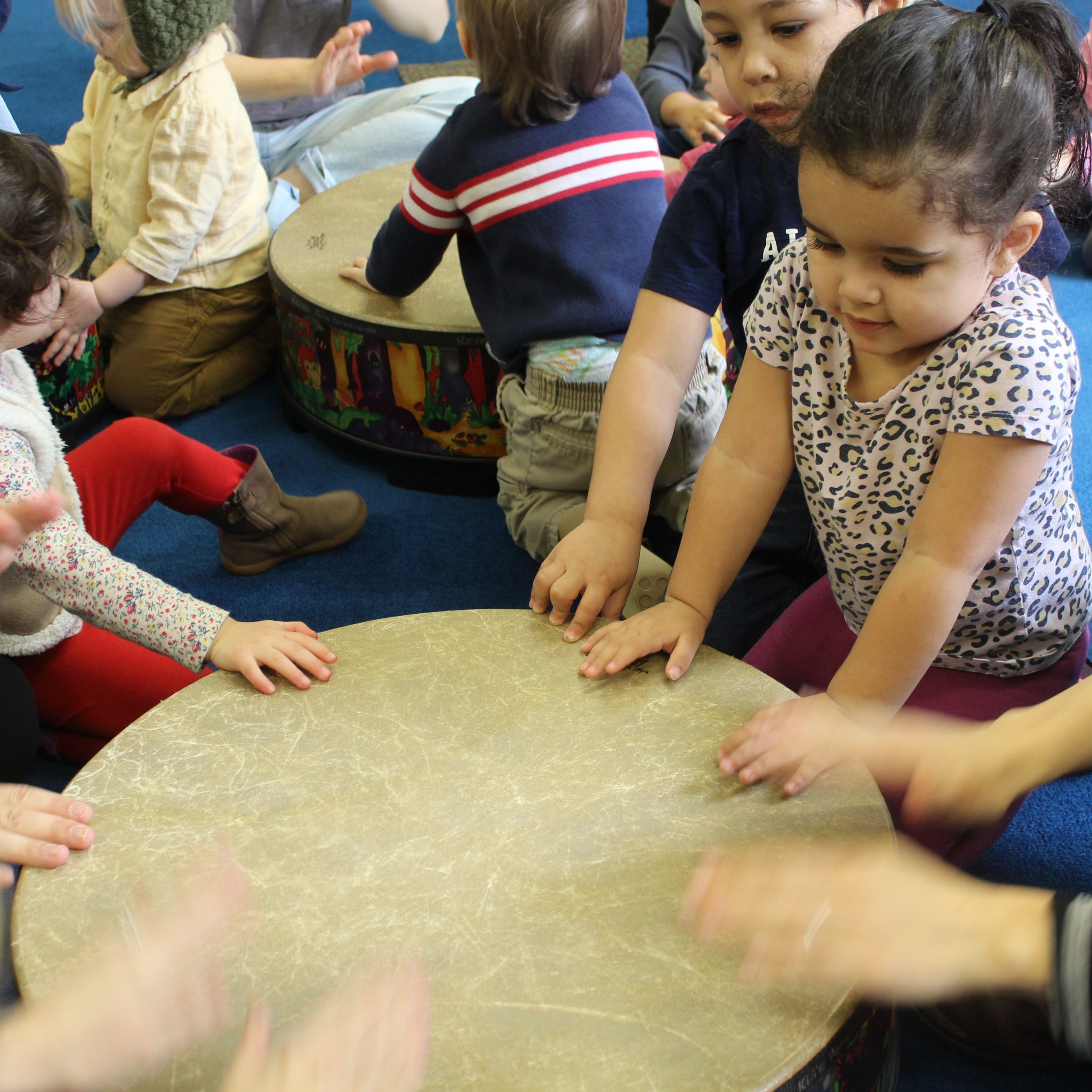 Prelude students playing big hand drums in a circle during a music class