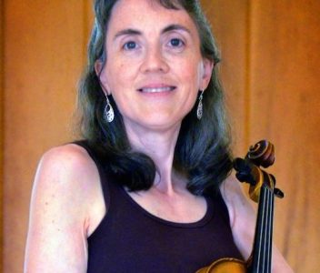 Headshot of Ann-Marie Messbauer holding her violin and smiling, visible from the waist and above