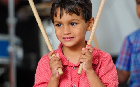 child holding up drum sticks and smiling
