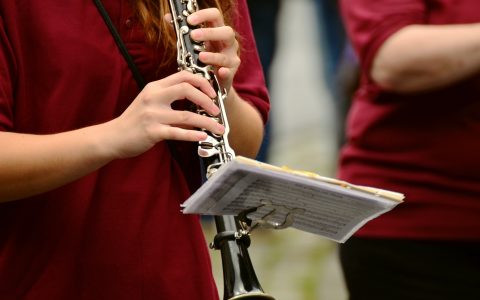someone's torso standing and playing a clarinet with a marching lyre attached