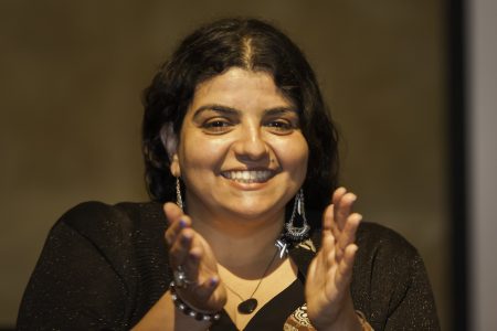 Eleni Yalanis clapping and smiling, showing from the shoulders and above, with a blurred background