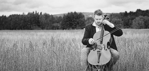 Karl Knapp playing the cello in a field, photo in black and white