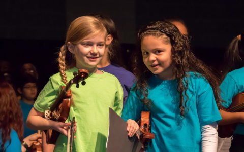 Close up of two Sonido string students holding their violins and smiling on stage at MLK performance