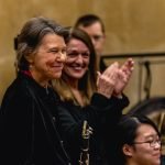 Mary Ellen Miller smiling and holding her clarinet in the YWES winter concert, Eileen McCaffery in the background clapping for her
