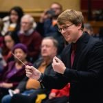 Assistant conductor of YWES leading them in their winter concert, blurred audience members in the background