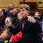 Assistant conductor of YWES leading them in their winter concert, blurred audience members in the background
