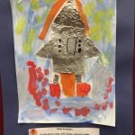 Prelude preschool art piece, a rocket made of tin foil in the middle, painting around it with a blue paper border