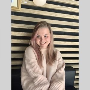 Daria Park sitting on a couch and smiling, showing from hips and above, wearing beige sweater