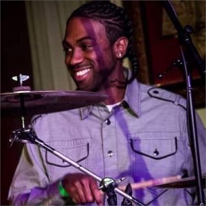 Trevor Pitts playing drum set and smiling