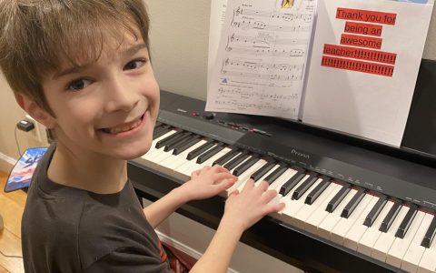 A valentine to CMSS faculty, Tommy Collins playing a keyboard turned around smiling, a note for teacher on the music stand