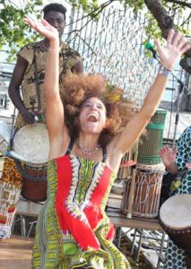 Tara dancing with her hands in the air and head thrown back with a drummer behind her