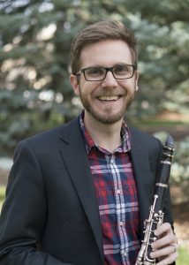 man with glasses standing holding clarine