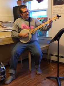 Man sitting on a piano bench playing a banjo