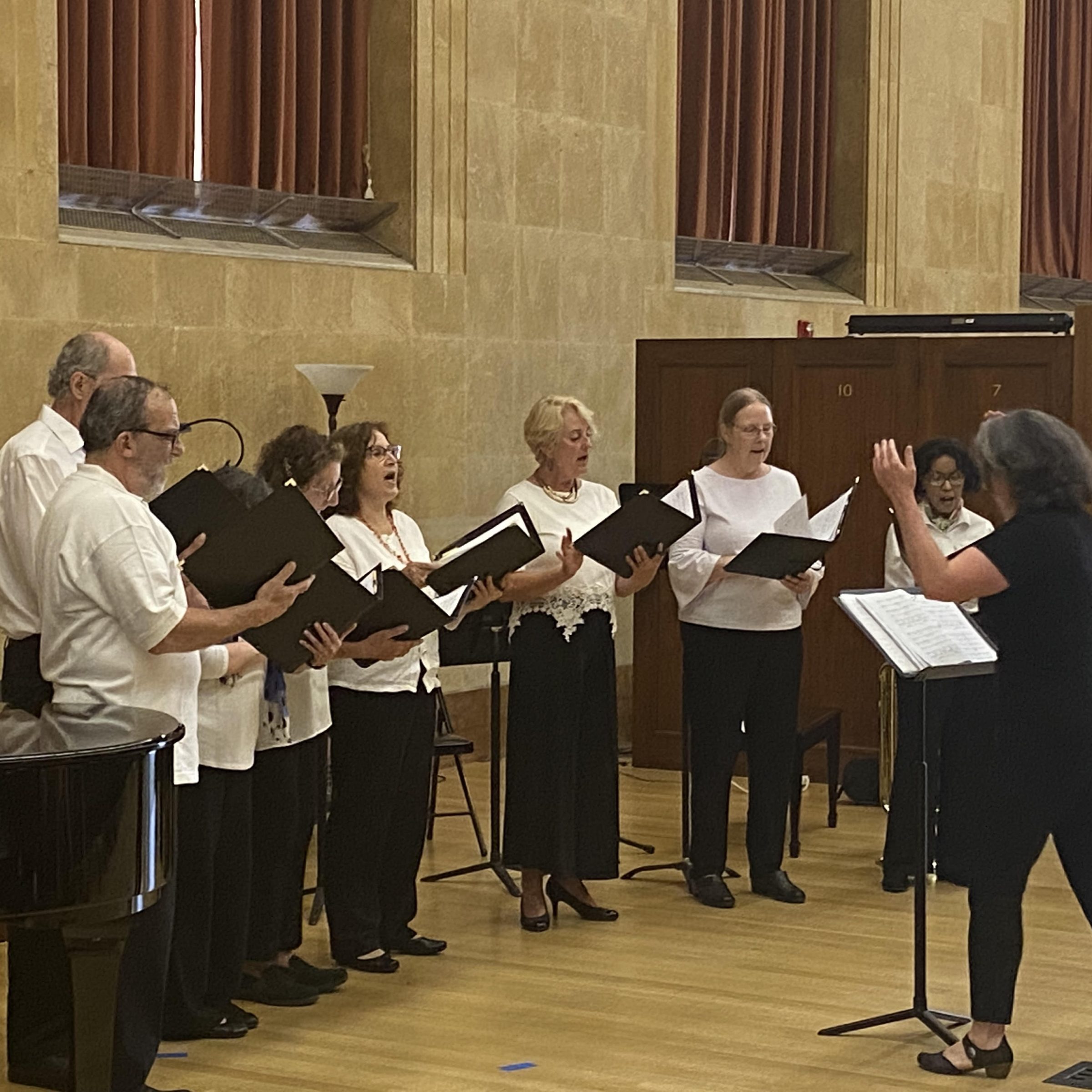 Group of adults in concert hall singing and holding folders with conductor directing them
