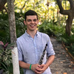 young man standing in wooded area holding oboe
