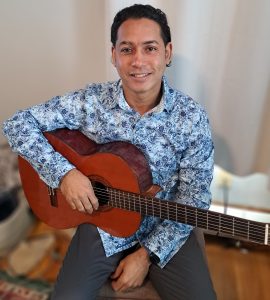 man sitting, holding guitar and smiling