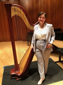 a person wearing a gray suit standing next to a harp on a stage and smiling with their hands in their jacket pockets