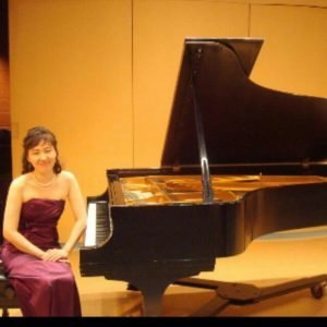 Woman in red dress sitting on piano bench next to a grand piano on a stage